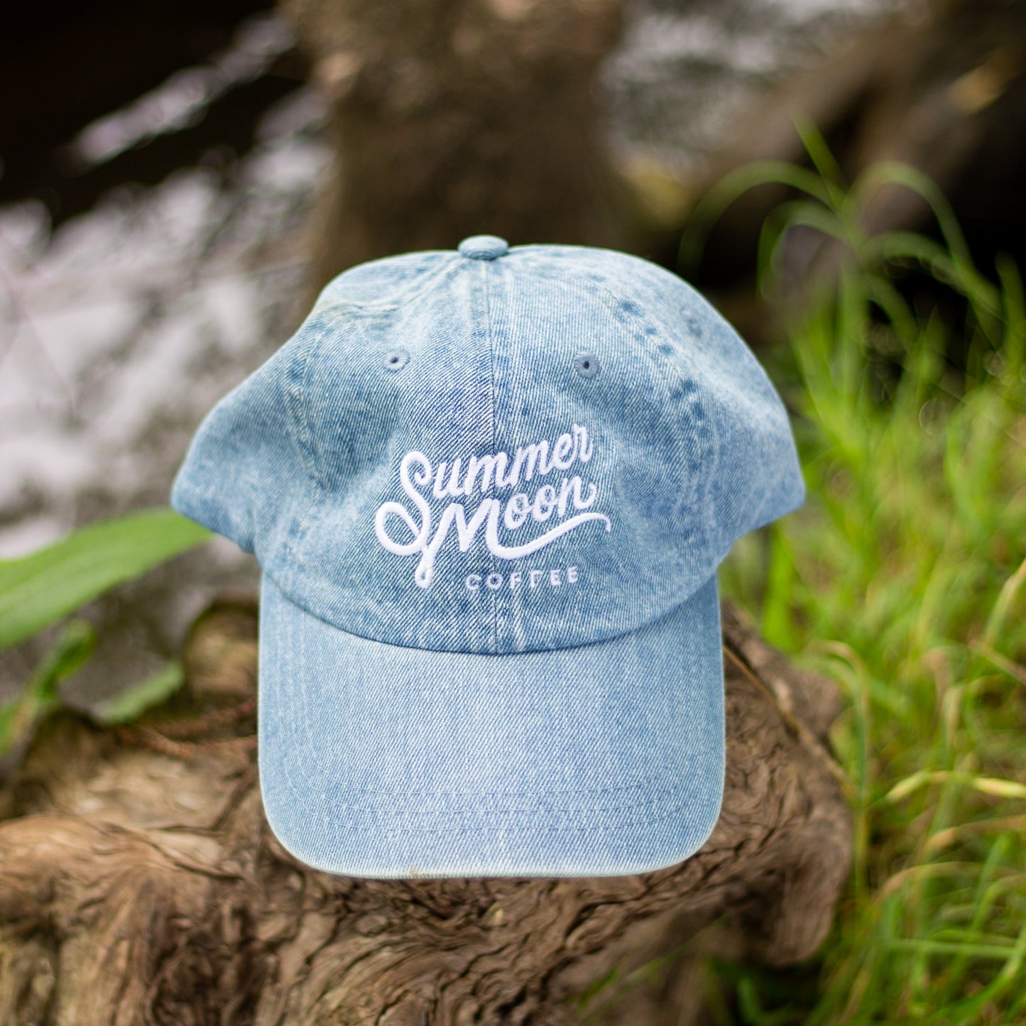 Light wash denim unstructured dad hat rests on a tree stump. 