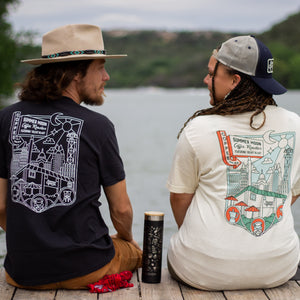 A couple sits on a pier wearing matching Summer Moon t-shirts in two color waves. 