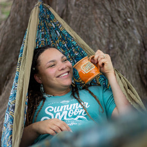 A woman sits in a hammock wearing a seafoam green Summer Moon graphic t-shirt.