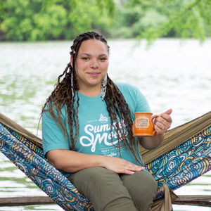 A woman sits in a hammock wearing a seafoam green Summer Moon graphic t-shirt.