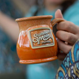 A orange glazed ceramic stoneware mug featuring the Summer Moon logo.