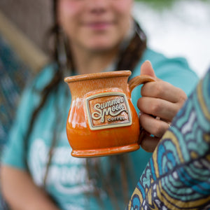 A orange glazed ceramic stoneware mug featuring the Summer Moon logo.